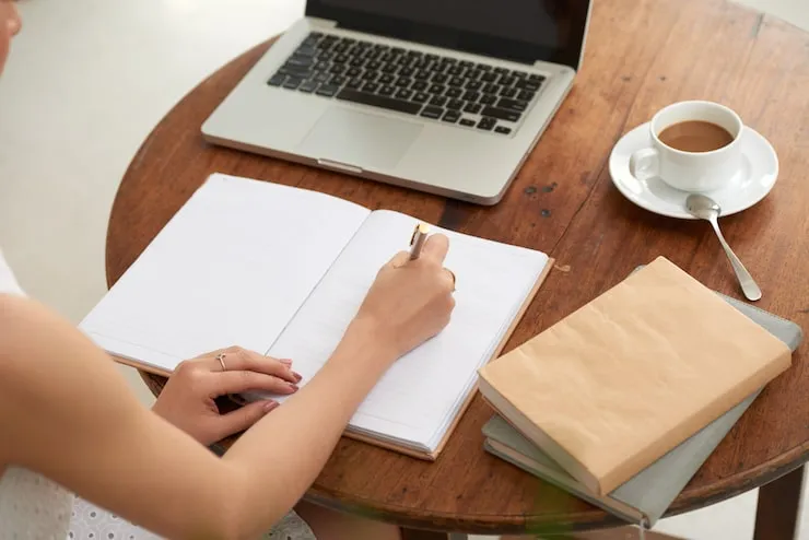Notizbuch, Laptop und Kaffee auf einem runden Holztisch