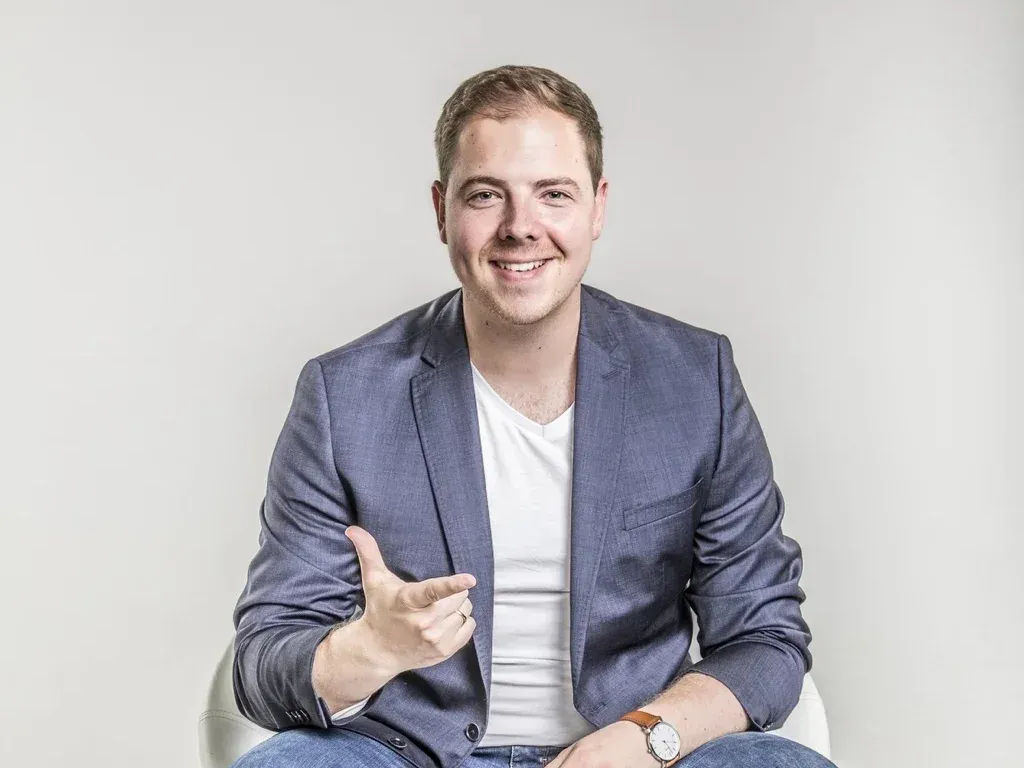 Jan Achnitz sitzt auf einem Hocker und erklärt mit einer Geste